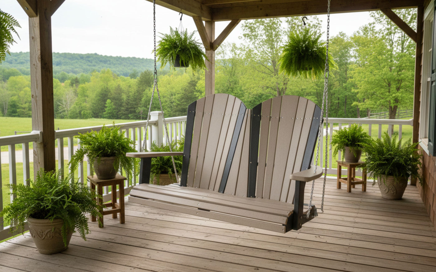 A black and weatherwood poly Amish made porch swing hangs on a front porch of a country home.